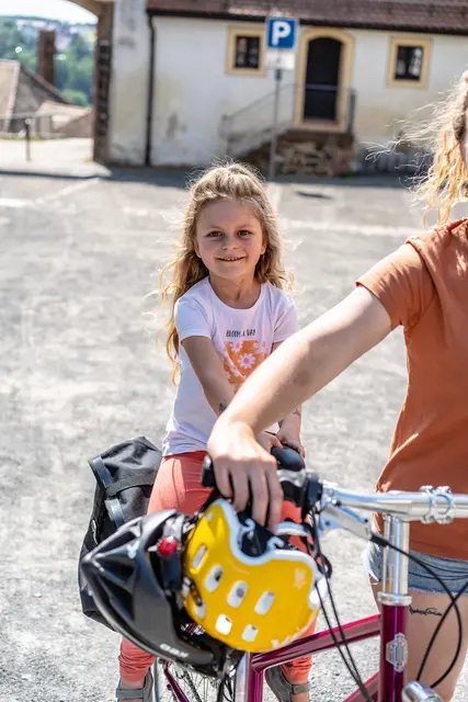 Ein Kind mit Fahrradhelm steht neben dem Familienfahrrad in einer Altstadt.