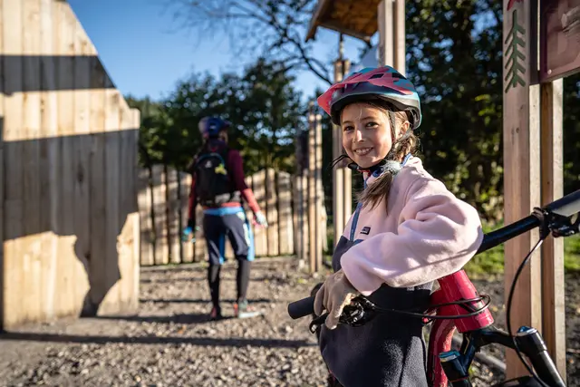 Ein Kind steht mit Mountainbike und Helm am Einstieg eines ausgeschilderten Trails.