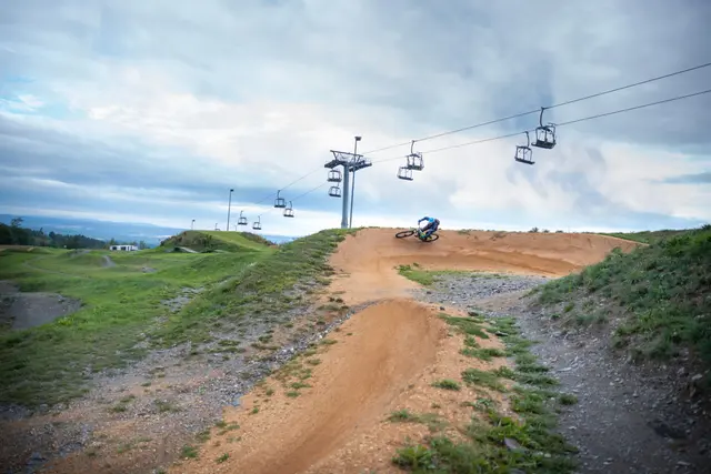 Ein Mountainbiker springt über eine Schanze unter einer Sesselbahn.