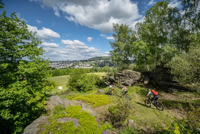 Mountainbiker fahren über Felsen mit weitem Blick über eine grüne Landschaft.