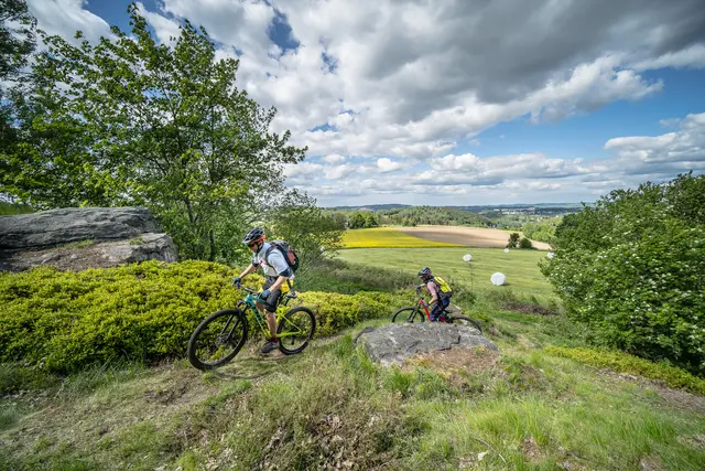 Ein Mountainbiker fährt über einen Felsentrail vor weiter Landschaft.