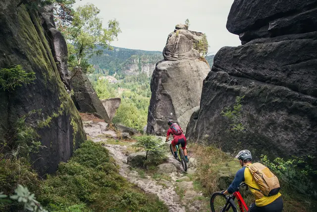 Zwei Mountainbiker fahren durch eine markante Felsenlandschaft im Wald.