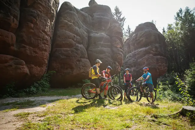 Eine Mountainbike-Gruppe macht Halt vor hohen Sandsteinfelsen.