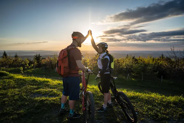 Zwei Mountainbiker geben sich vor dem Sonnenuntergang ein High Five.