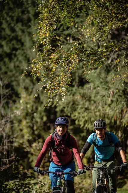 Zwei Mountainbiker fahren im Hochformat durch einen dunklen Wald.