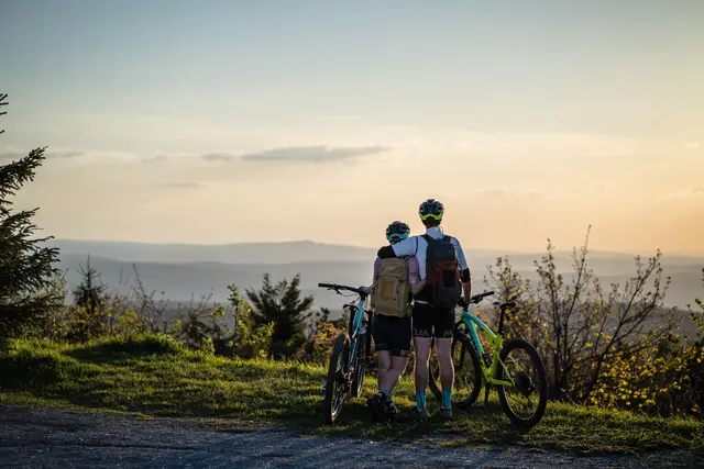 Drei Mountainbiker blicken bei tief stehender Sonne über das Erzgebirge.