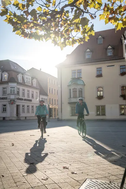 Eine Radfahrerin fährt im Gegenlicht durch einen historischen Stadtkern.
