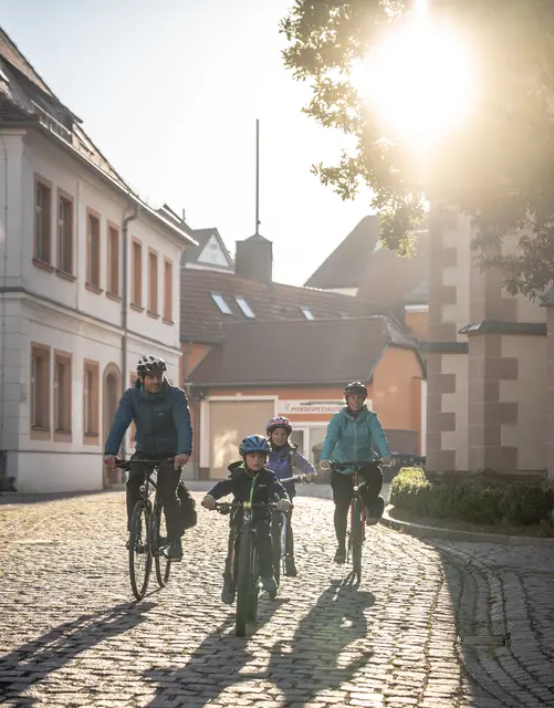 Eine Radgruppe fährt im warmen Morgenlicht durch eine gepflasterte Altstadtgasse.