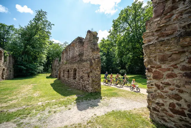 Eine Radgruppe fährt zwischen den Mauern einer historischen Ruine hindurch.