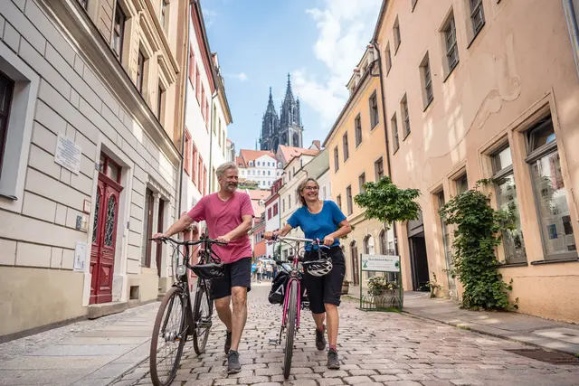 Ein Radpaar schiebt seine Fahrräder durch eine Gasse der Meißner Altstadt.