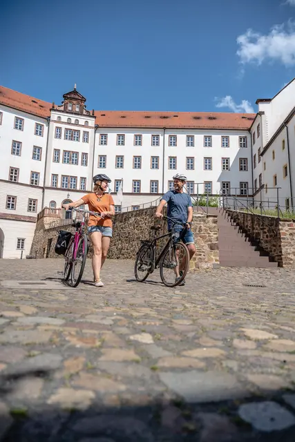 Zwei Radgäste stehen mit ihren Fahrrädern auf einem historischen Schlossplatz.