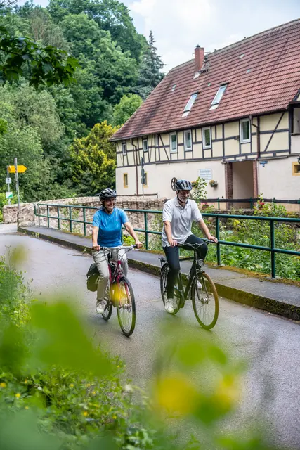 Zwei Radgäste fahren über eine überdachte Holzbrücke.