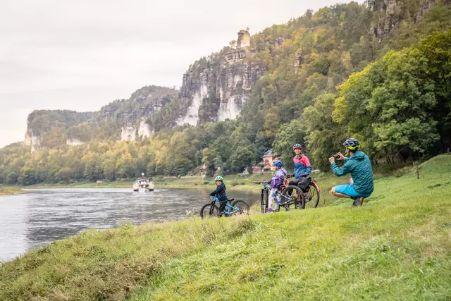 Eine Familie macht am Elbufer unterhalb markanter Felsen eine Radtourpause.