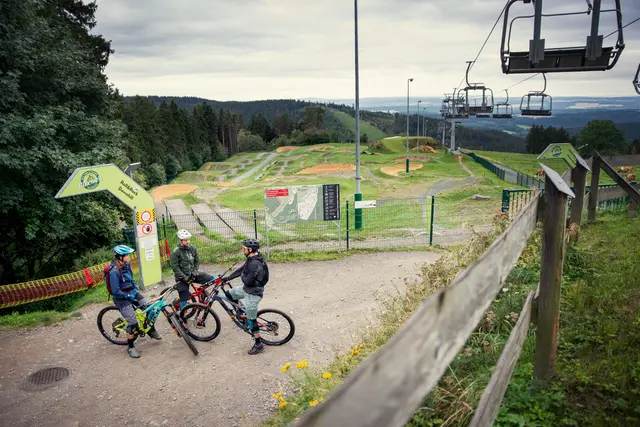 Mountainbiker stehen am Einstieg des Bikeparks Schöneck unter einer Sesselbahn.