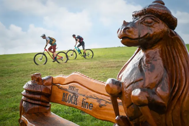 Zwei Mountainbiker passieren eine geschnitzte Holzfigur mit dem Schriftzug Rock the line.